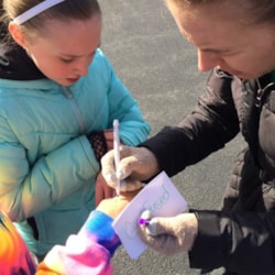 Girls on the run coach writes on a participant's hand during an outdoor practice.